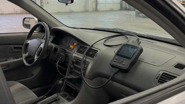 Diagnostic scan tool beside a parked vehicle with its check engine light illuminated