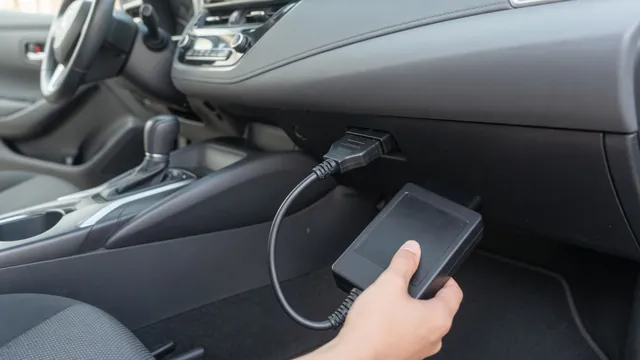 Handheld OBD-II scan tool connected to a car's diagnostic port under the dashboard