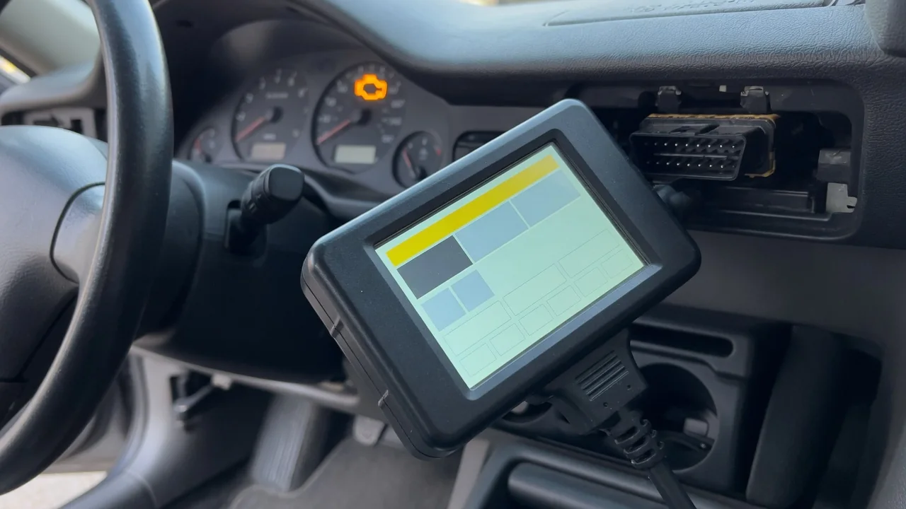OBD-II scan tool plugged into a car's diagnostic port, with the check engine light on in the background
