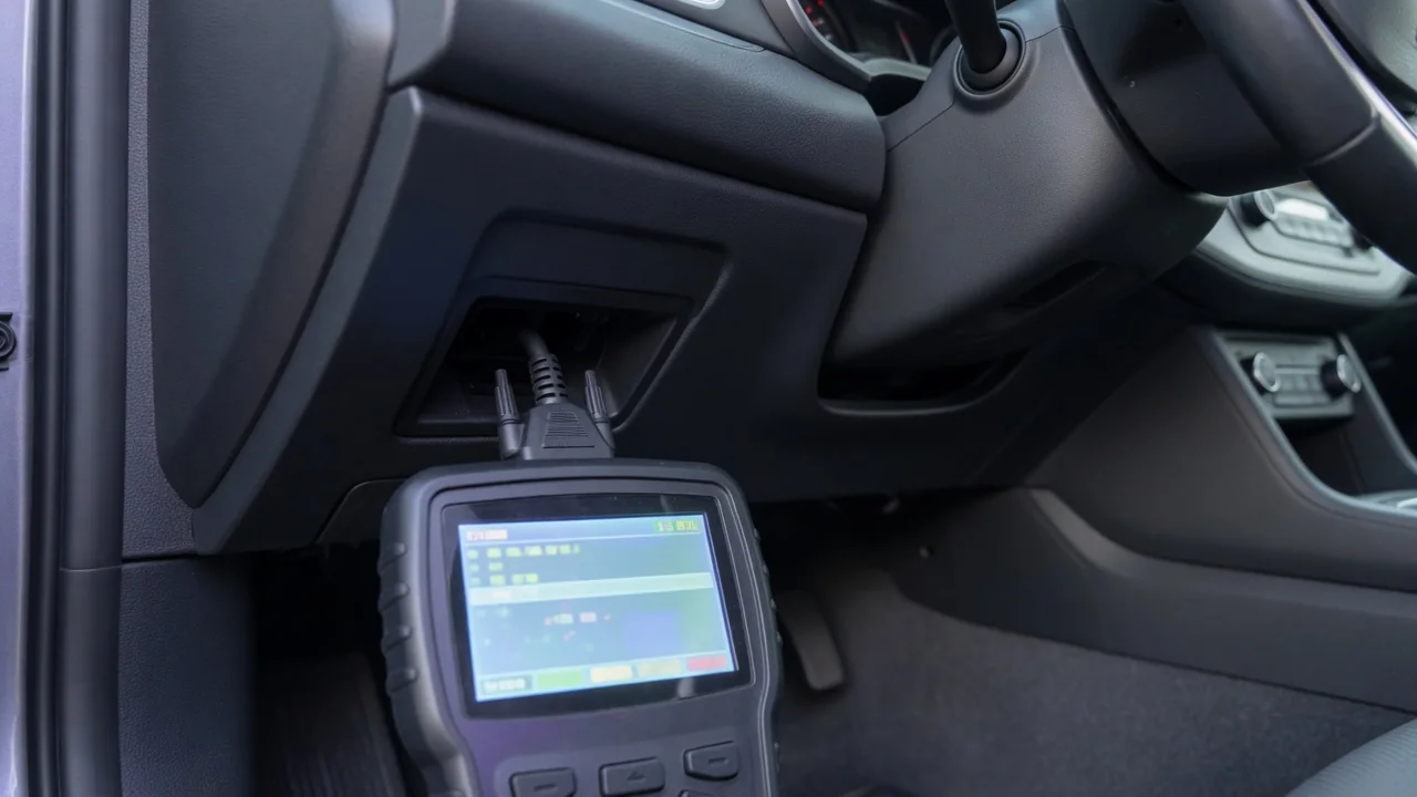 Handheld OBD-II scanner connected under a car dashboard to read a manufacturer-specific trouble code