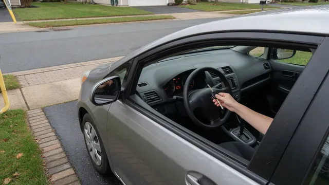 Driver holding a car key beside the steering column of a compact hatchback that won't start