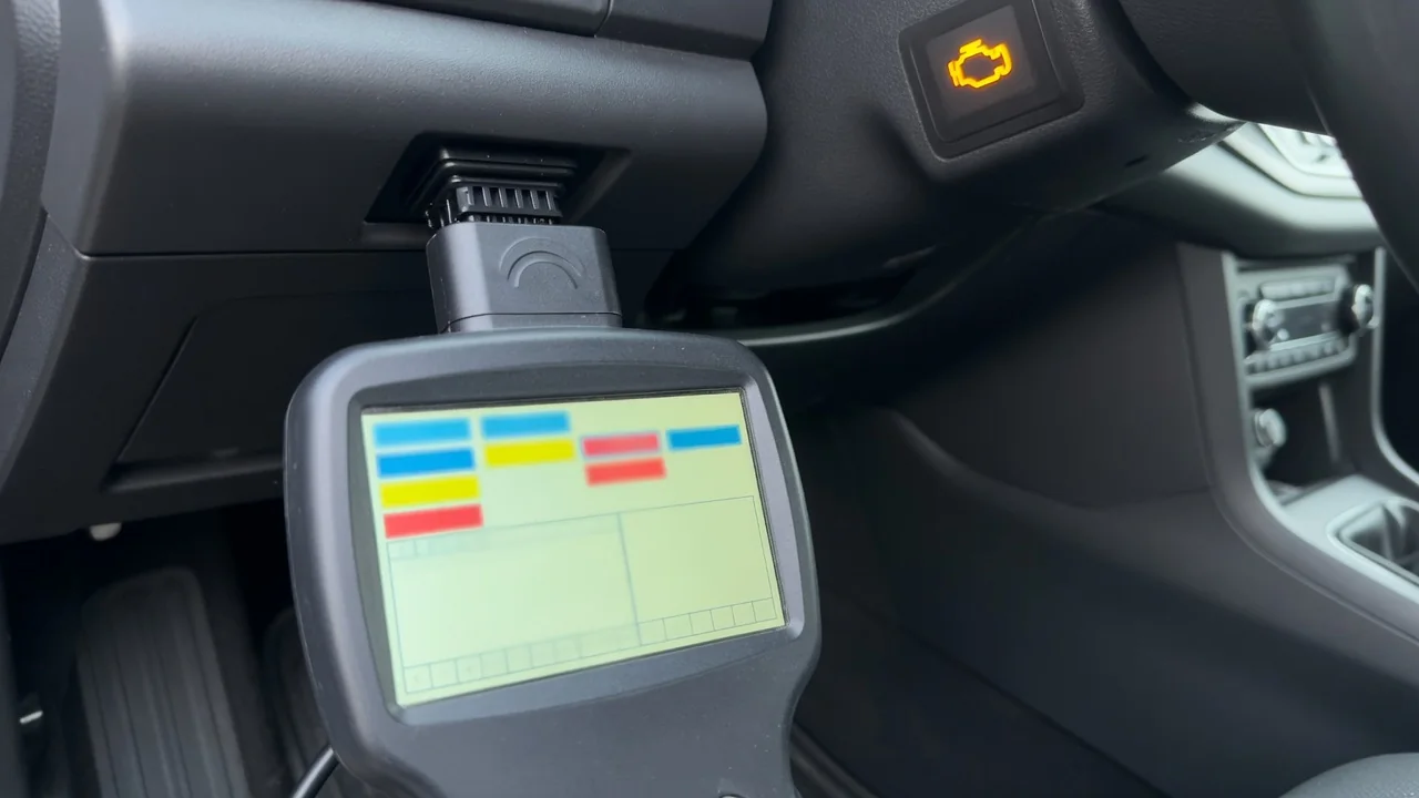 OBD-II scan tool plugged in under a car dashboard with the check engine light on, reading a trouble code