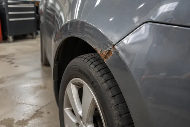 Close-up of rust bubbling beneath chipped paint along a car wheel arch