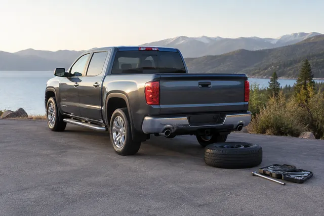 Pickup spare tire on level pavement beside a spare tire tool kit and lock key