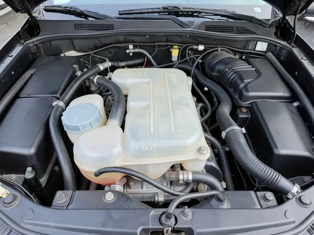 Translucent coolant reservoir with level markings, a closed cap, and attached hoses in an engine bay