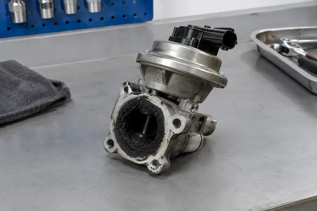 EGR valve on a workshop bench with visible carbon deposits around its opening