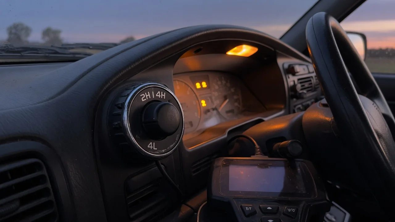 Truck dashboard with a 4WD selector knob, warning lights on, and an OBD-II scan tool plugged in