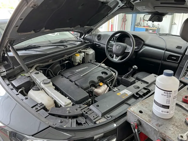 Engine oil dipstick and an unbranded additive bottle beside an open engine bay