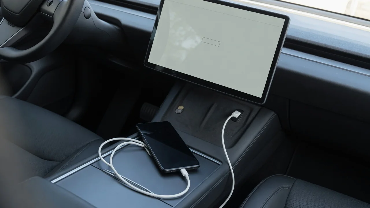 Android phone plugged into a car's dashboard USB port with a cable, infotainment screen in the background