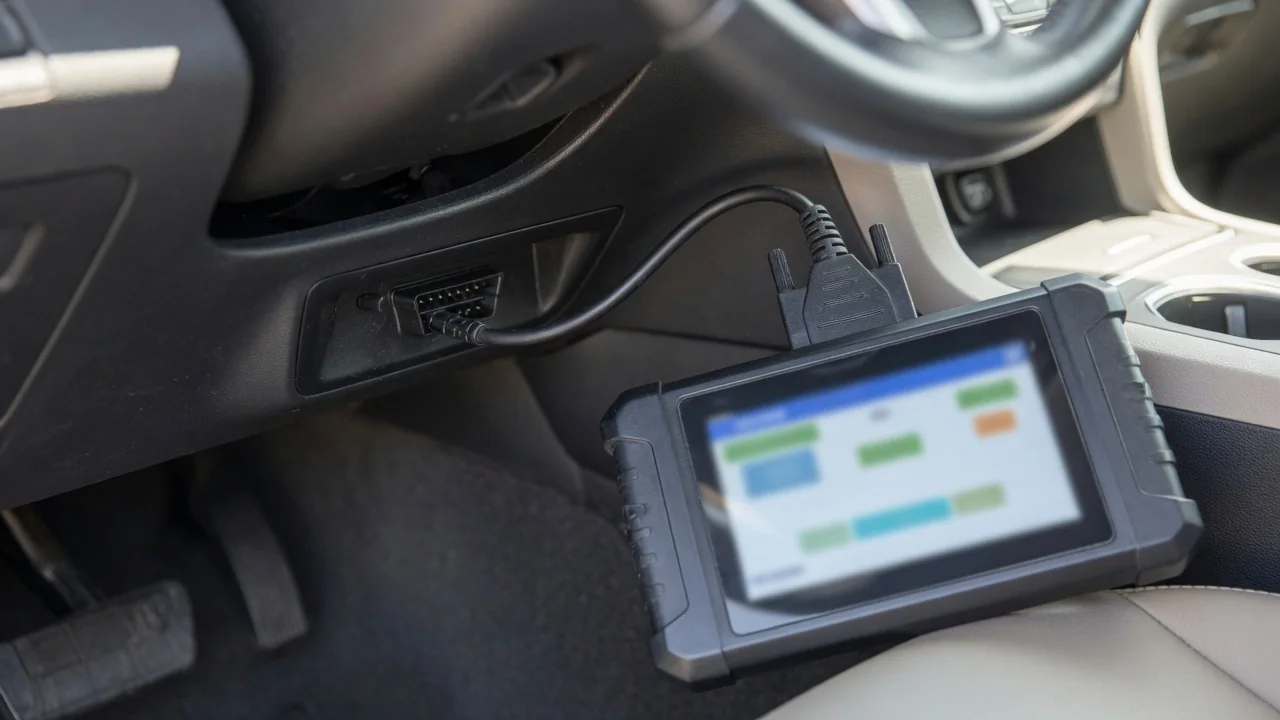 Handheld OBD-II scanner plugged into a car's diagnostic port under the dashboard to read a trouble code