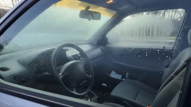 Condensation beads on the inside of a parked car’s windshield and side window on a cool morning.