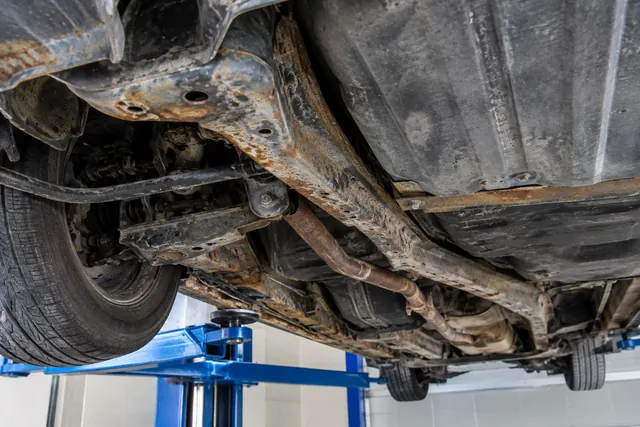 Car underbody showing rust along a frame rail and nearby mounting areas during a professional inspection.