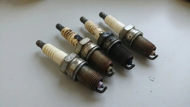 Removed spark plugs showing pale insulators, dry carbon deposits, electrode damage, and exterior rust.
