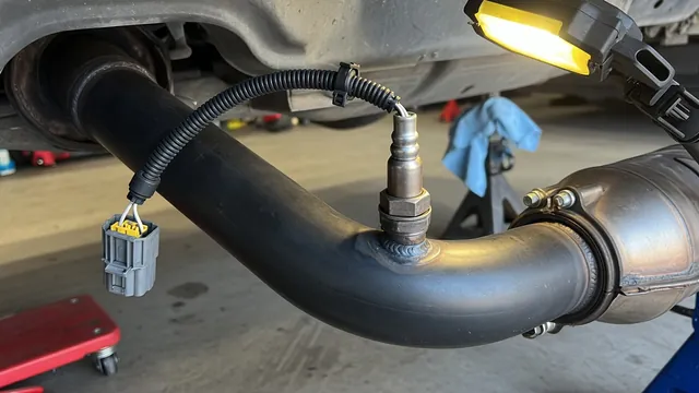 Oxygen sensor installed in a car exhaust pipe with its wiring connector visible