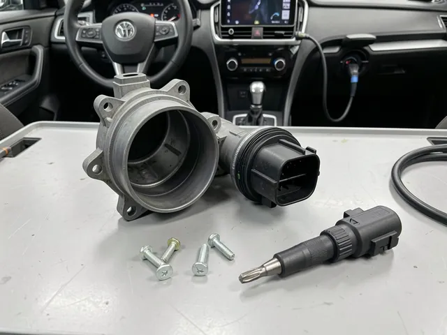 Mass air flow sensor beside an intake housing with mounting screws and a matching driver