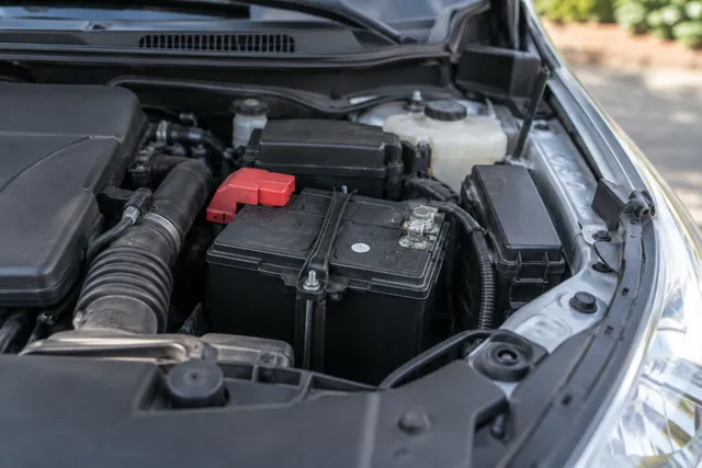 A 12-volt car battery in an open engine bay with its date-code sticker and terminals visible