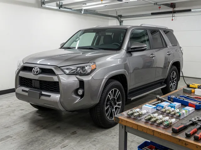 Spark plugs and ignition service tools arranged beside a Toyota 4Runner in a garage