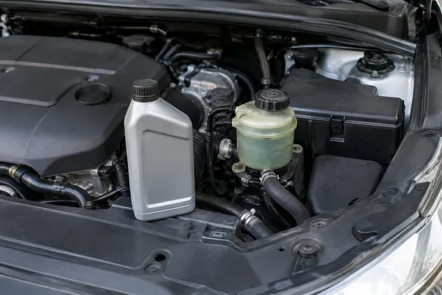Power steering fluid bottle beside a hydraulic steering reservoir in an engine bay