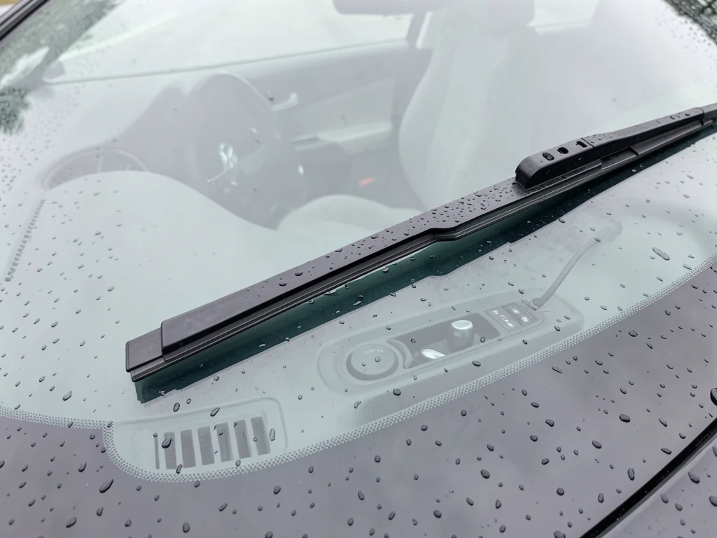 Windshield wiper blade resting on a clean windshield dotted with rain