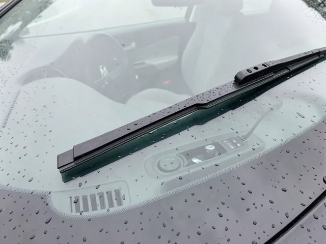 Windshield wiper blade resting on a clean windshield dotted with rain