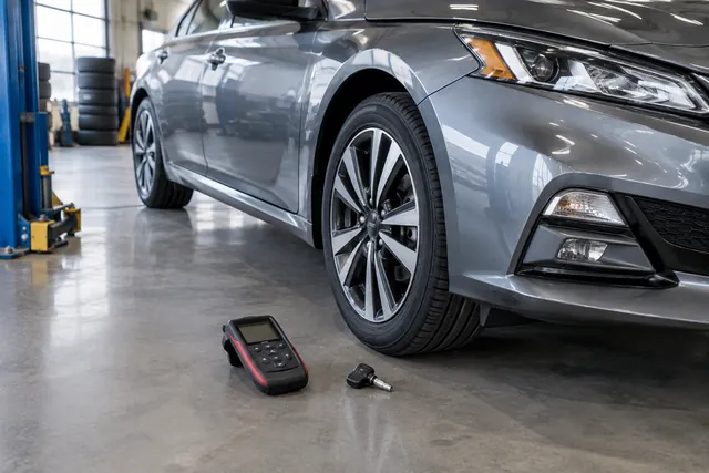 Nissan Altima wheel with a TPMS sensor and handheld diagnostic tool nearby