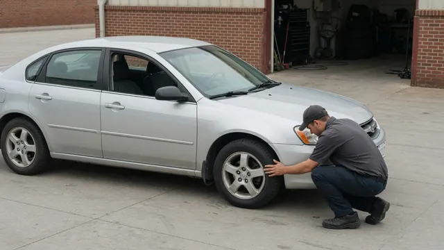 Car parked on level pavement with a technician inspecting a front tire and wheel