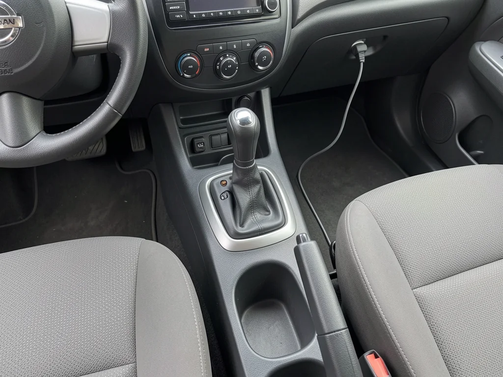 Manual gearshift and three pedals inside a parked car with an unbranded interior.