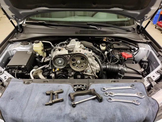 Power steering pump with pulley and fluid reservoir in an engine bay, with a pulley puller and wrenches laid out for replacement