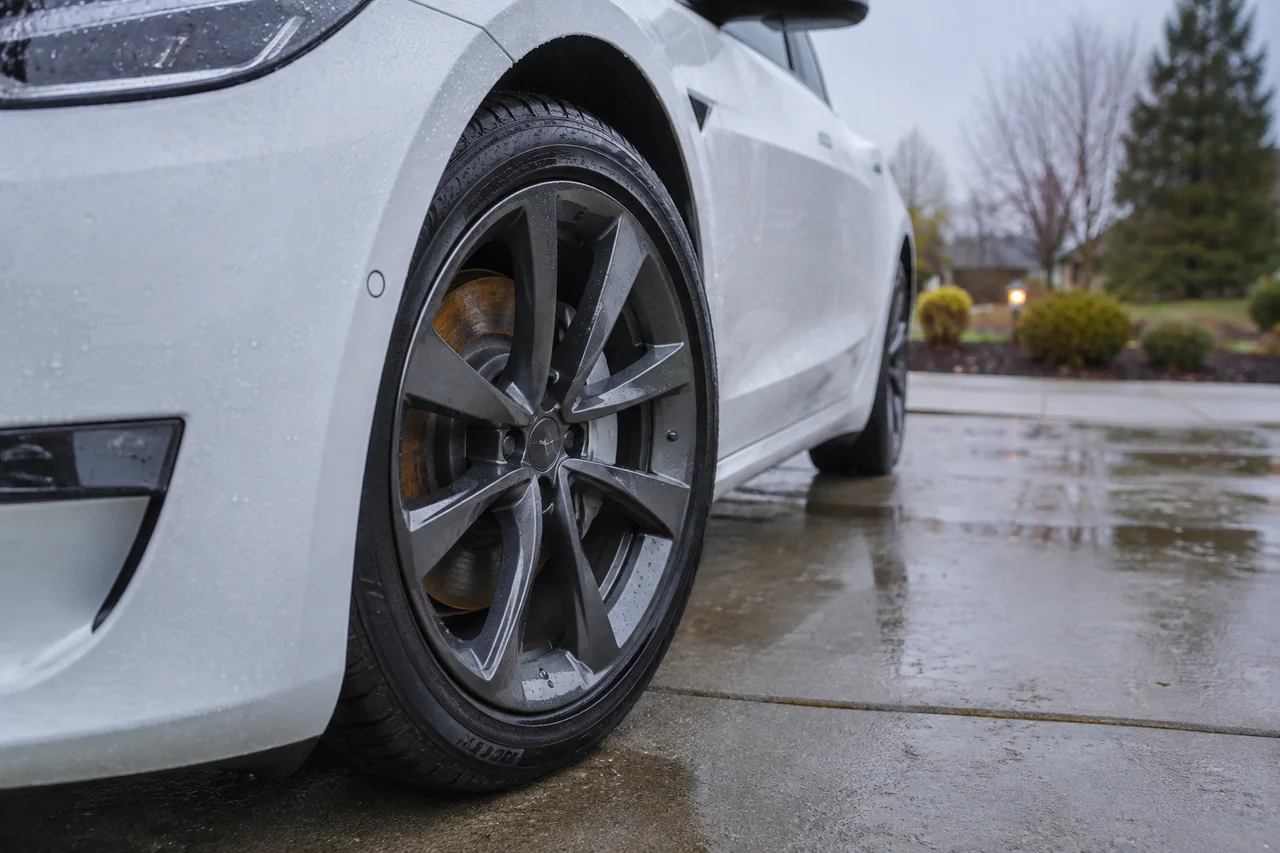 Brake rotor with light surface rust seen through the wheel spokes of an electric sedan parked on a wet driveway