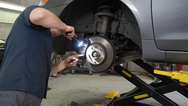 Technician inspecting an exposed wheel hub and bearing area with a flashlight in an automotive workshop