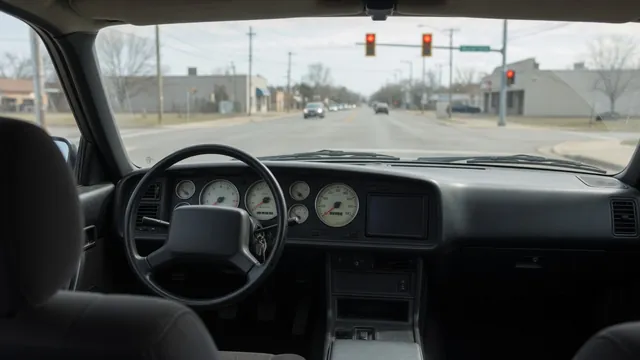 Dashboard tachometer near zero in a parked car with a red traffic light visible ahead
