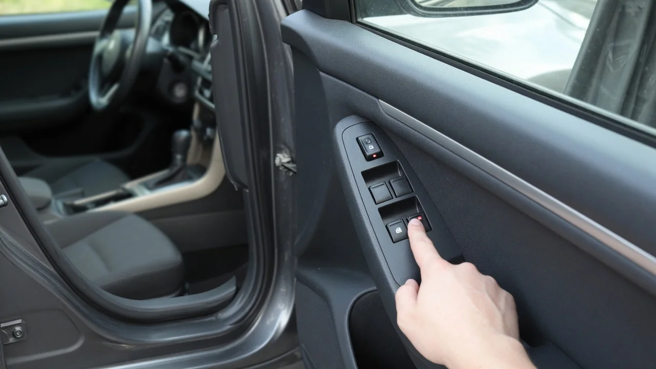 Driver's hand pressing the power door lock switch on a car door panel