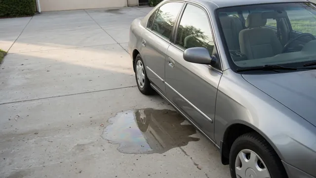 Small clear puddle beneath the front passenger area of a parked car on a dry driveway