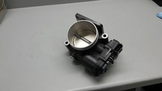 Automotive throttle body with its circular opening and throttle plate visible on a workbench
