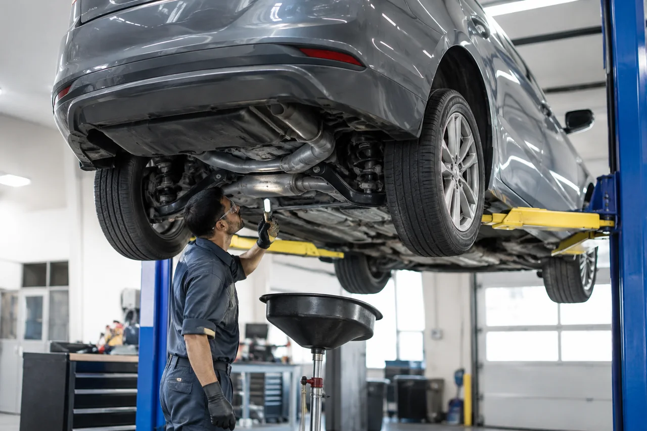 Technician inspecting the underside of a midsize sedan on a shop lift during a differential fluid check
