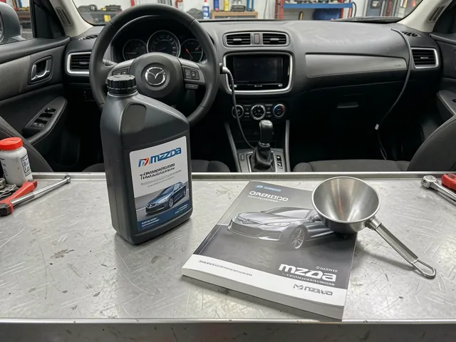Transmission fluid bottle beside a Mazda owner’s manual and a clean service funnel