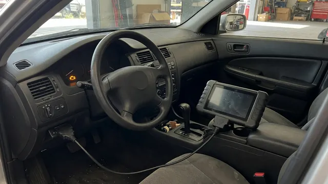 Diagnostic scanner beside a parked vehicle with a check engine warning visible on the dashboard