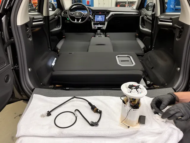 New fuel pump module and seal placed next to an open under-seat access panel in a car during replacement