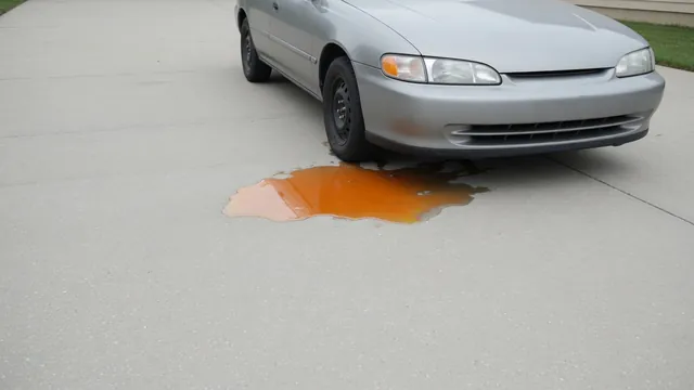 Orange fluid puddle beneath the front of a parked car on a concrete driveway
