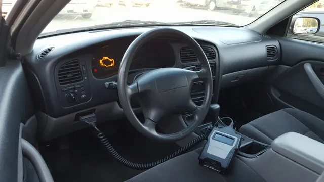 Ford dashboard with an illuminated check engine light and an OBD-II scanner beside the steering wheel