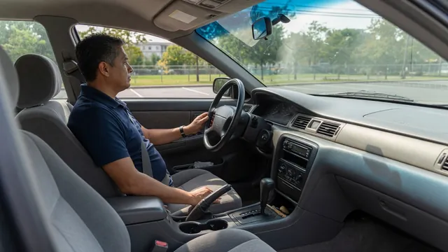 Driver seated in a parked car with hands on the steering wheel and the dashboard visible