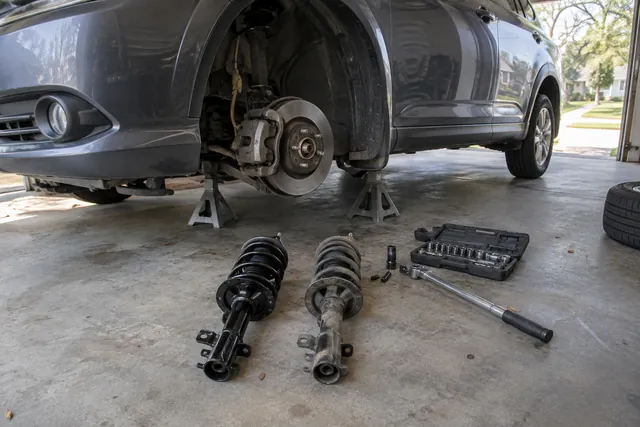 Car on jack stands with front wheel removed, new strut and old shock absorber beside a torque wrench