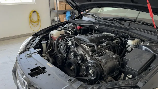 Car engine bay showing the accessory belt and AC compressor that adds load to the engine at idle