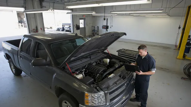 GM truck in a service bay with its hood open and a technician reviewing engine diagnostic readings
