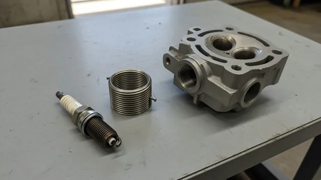 Spark plug, threaded insert, and cylinder head spark plug opening on a clean workbench
