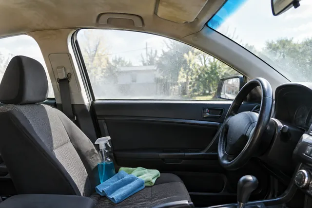 Microfiber towels and automotive glass cleaner beside a car window and lightly stained fabric headliner