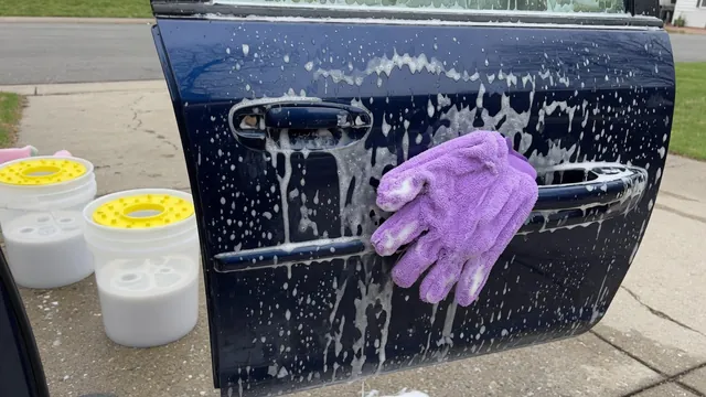 Foamy car shampoo on a car door with a microfiber wash mitt and two wash buckets in the background