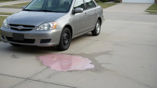 Small pink fluid puddle beneath the front of a parked car on a dry driveway