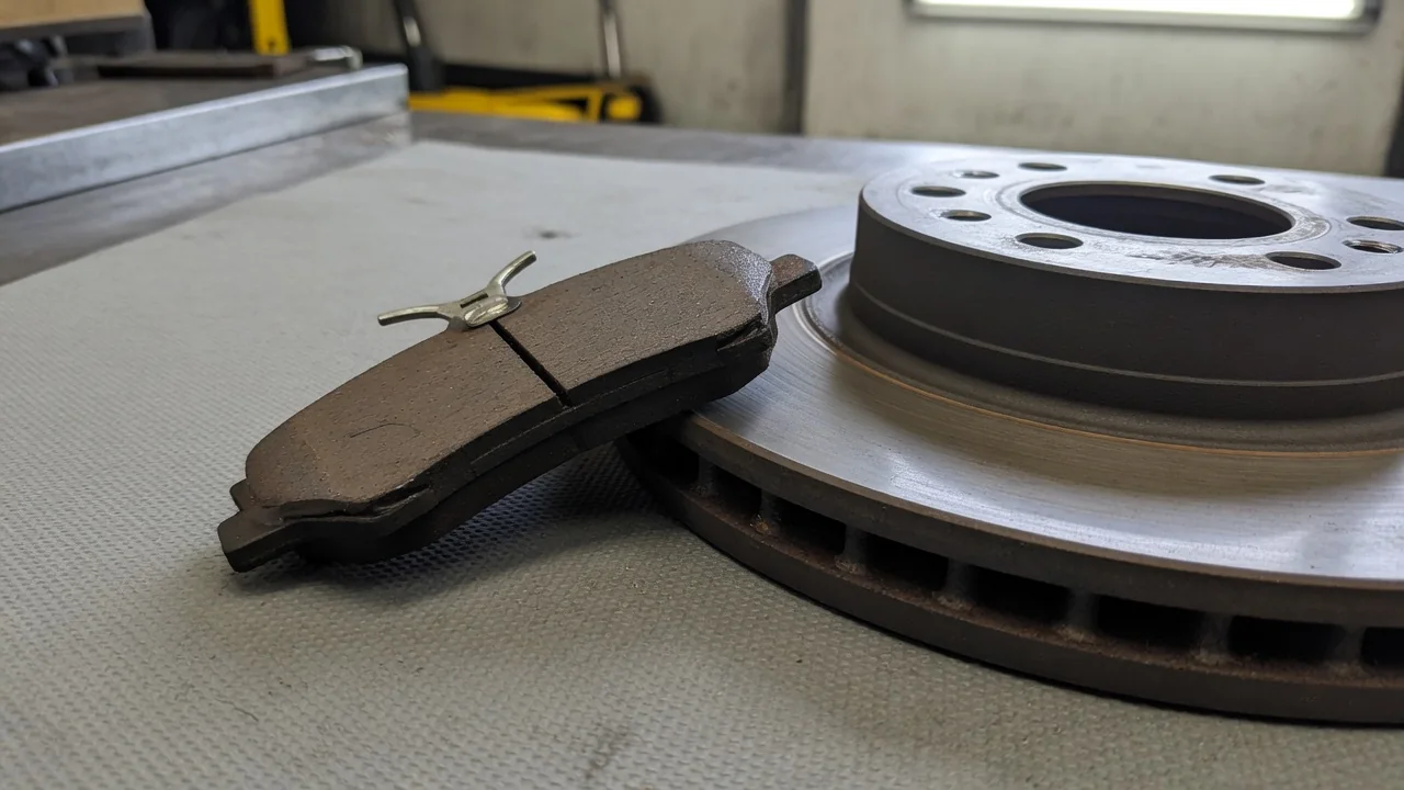 Brake pad with its metal wear-indicator tab visible beside a brake rotor