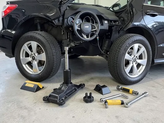 Tire rotation tools arranged beside a parked car, including a floor jack, jack stands, wheel chocks, and torque wrench.